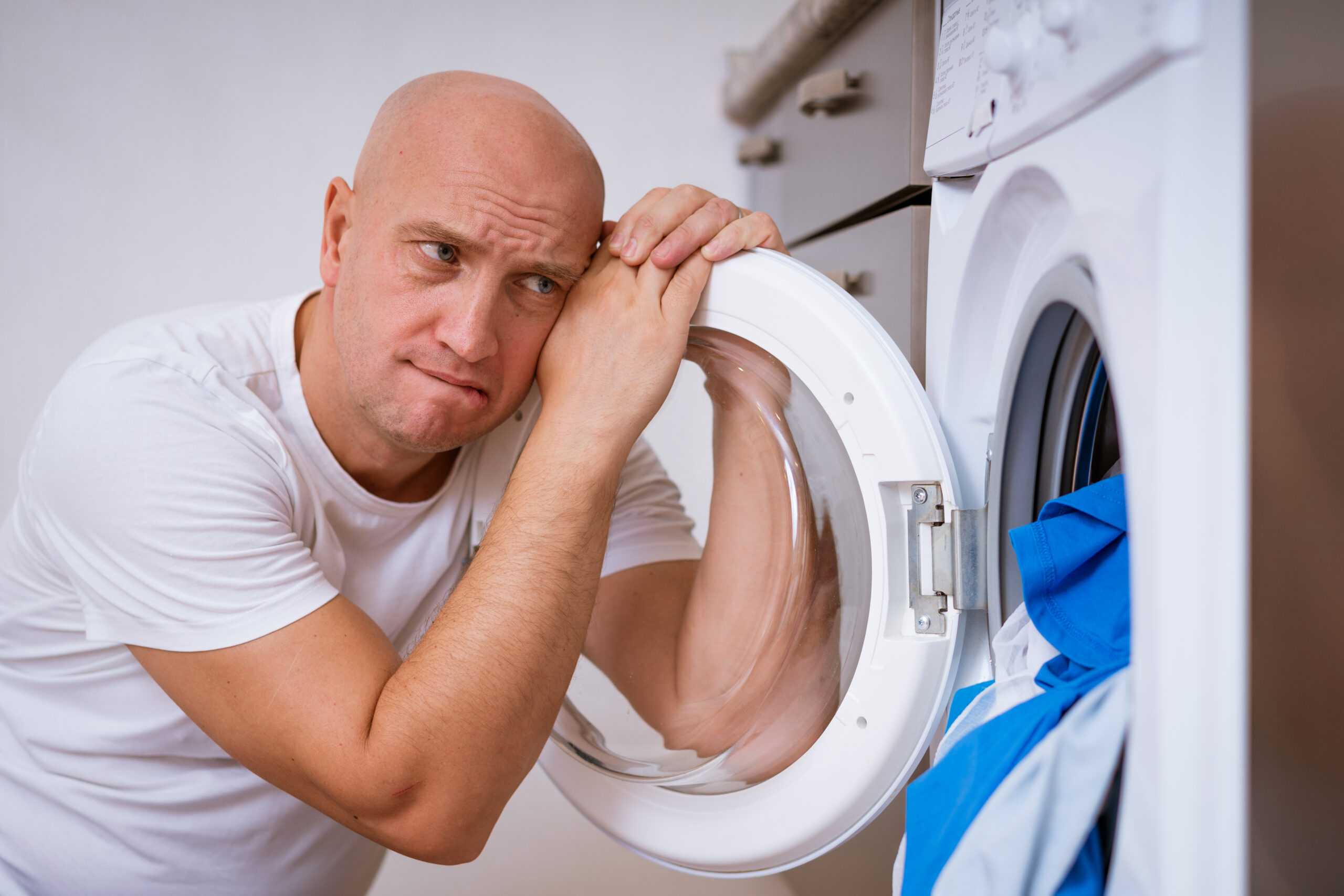 tired bald man sitting with dirty laundry in the washing machine. Cleaning concept