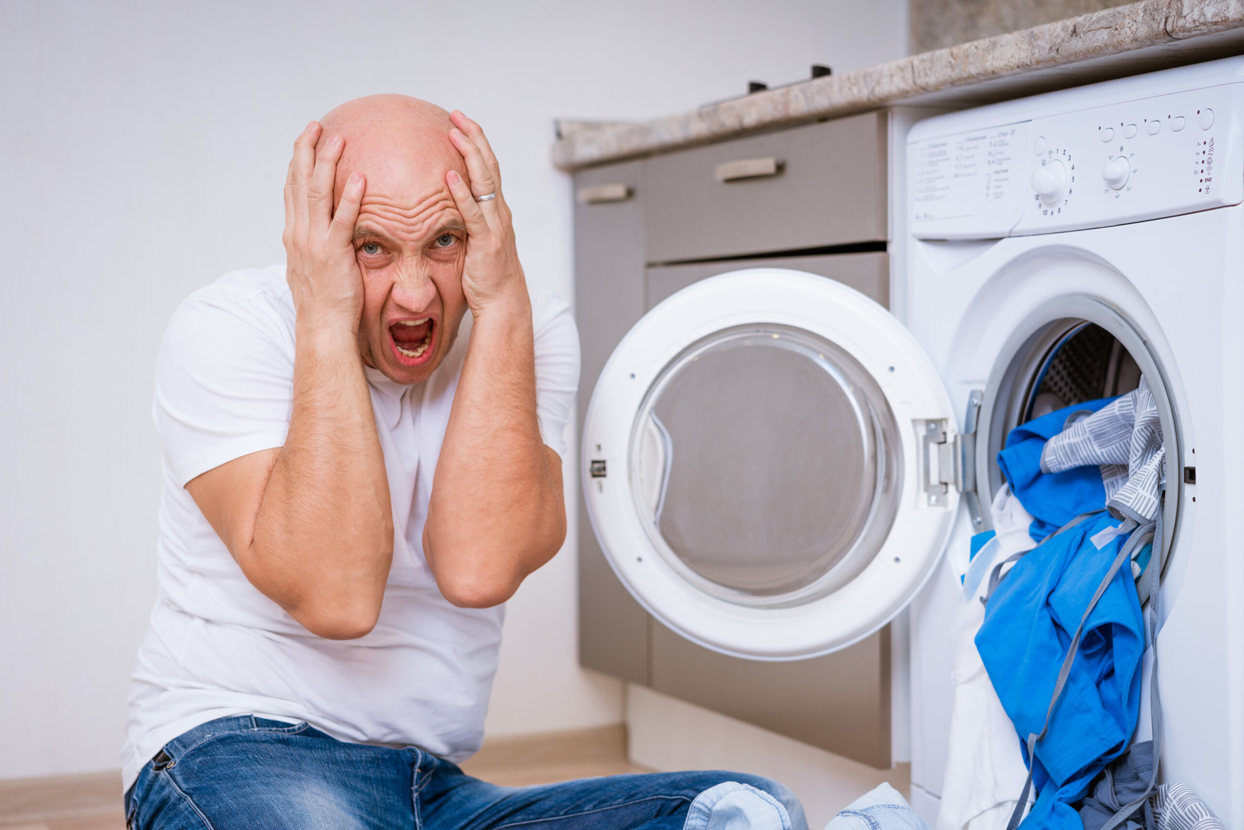 tired man sits with laundry at the washing machine